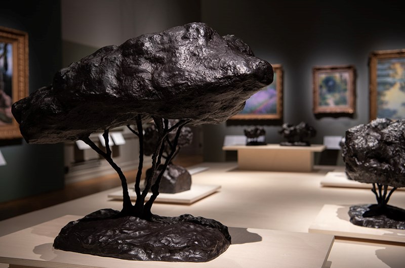 Interiörbilder från utställningen Trädgården på Nationalmuseum med skulpturer ”Porträtt av en skog, träd” av Peter Fries i förgrunden